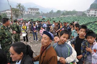 People stand in a line to get suppers at a temporary resettlement for the earthquake victims in Baoshan Village in Longmenshan Township of Pengzhou City, southwest China's Sichuan Province, May 25, 2008. (Xinhua/Hao Tongqian)