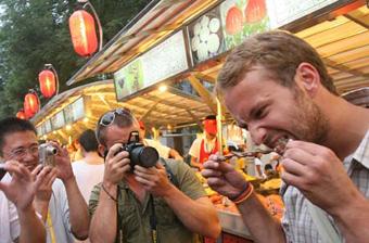A foreign tourist tries a Chinese snack at the Donghuamen night fair in Beijing, capital of China, Aug. 13, 2008. The night fair selling more than 100 kinds of delicious snacks from across China, has become an attraction to foreign tourists during the Beijing 2008 Olympic Games.(Xinhua Photo/Chen Xiaogen)