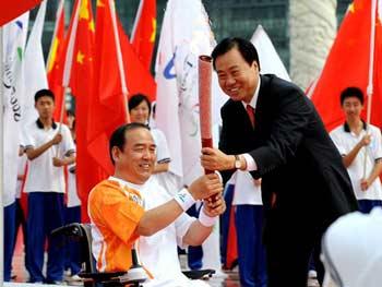 Xia Deren (R), mayor of Dalian, passes a Beijing Paralympic torch to wheelchair-bound Li Yang to kick off the Dalian leg of the torch relay on September 3, 2008.[Photo: Xinhua]