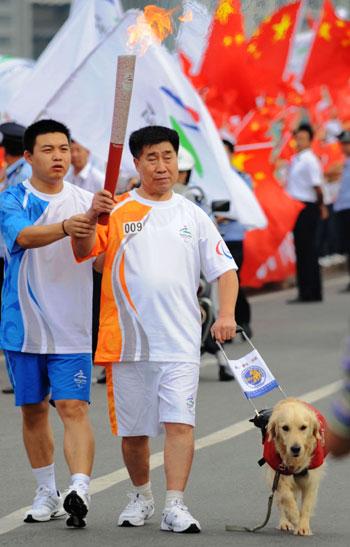 Zhang Dehong (right) holds the Paralympic torch with the help of a torch escort and a guide dog during the Dalian relay on Wednesday. 