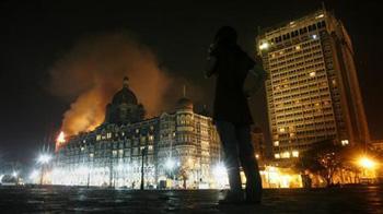 A reporter talks on her phone as smoke is seen coming from Taj Hotel in Mumbai November 27, 2008. (Xinhua/Reuters Photo)