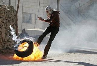 A masked Palestinian youth kicks a burning tire in the West Bank city of Hebron during a protest against the occupation of a disputed house by Jewish settlers.(AFP/Hazem Bader)