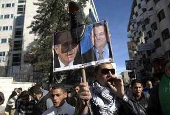 A Palestinian holds up a placard with pictures of Israel's Prime Minister Ehud Olmert (L) and Defence Minister Ehud Barak, during a protest in the West Bank city of Ramallah against Israel's offensive in Gaza, January 5, 2009.REUTERS/Fadi Arouri (WEST BANK) 