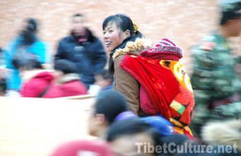 A woman who carries a baby on her back smiles while waiting for her train.(Photo: tibetculture.net)