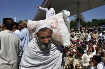 A man internally displaced from Swat Valley carries a sack of wheat flour as other wait their turn at a relief camp arranged a Pakistani political party in Mardan, Pakistan Sunday, May 10, 2009. Thousands of fearful civilians, many on foot or donkey-pulled carts, streamed out of a conflict-ridden Pakistani valley Sunday as authorities briefly lifted a curfew. The army said it had killed scores of militants in the latest fighting.(AP Photo/Mohammad Sajjad)