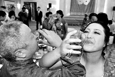 51-year-old bridegroom Zhang Mingliang (left) and 43-year-old bride Pu Xiaorong (right) cross their arms to drink wine on July 13. On the same day, 15 couples from Sichuan quake-hit regions held a wedding ceremony in Beijing.